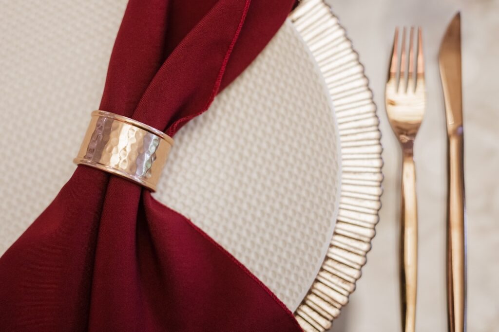 Fall Wedding Color Palettes That Work Beautifully at The Embassy 1 a burgundy napkin in a golden holder laying on a plate
